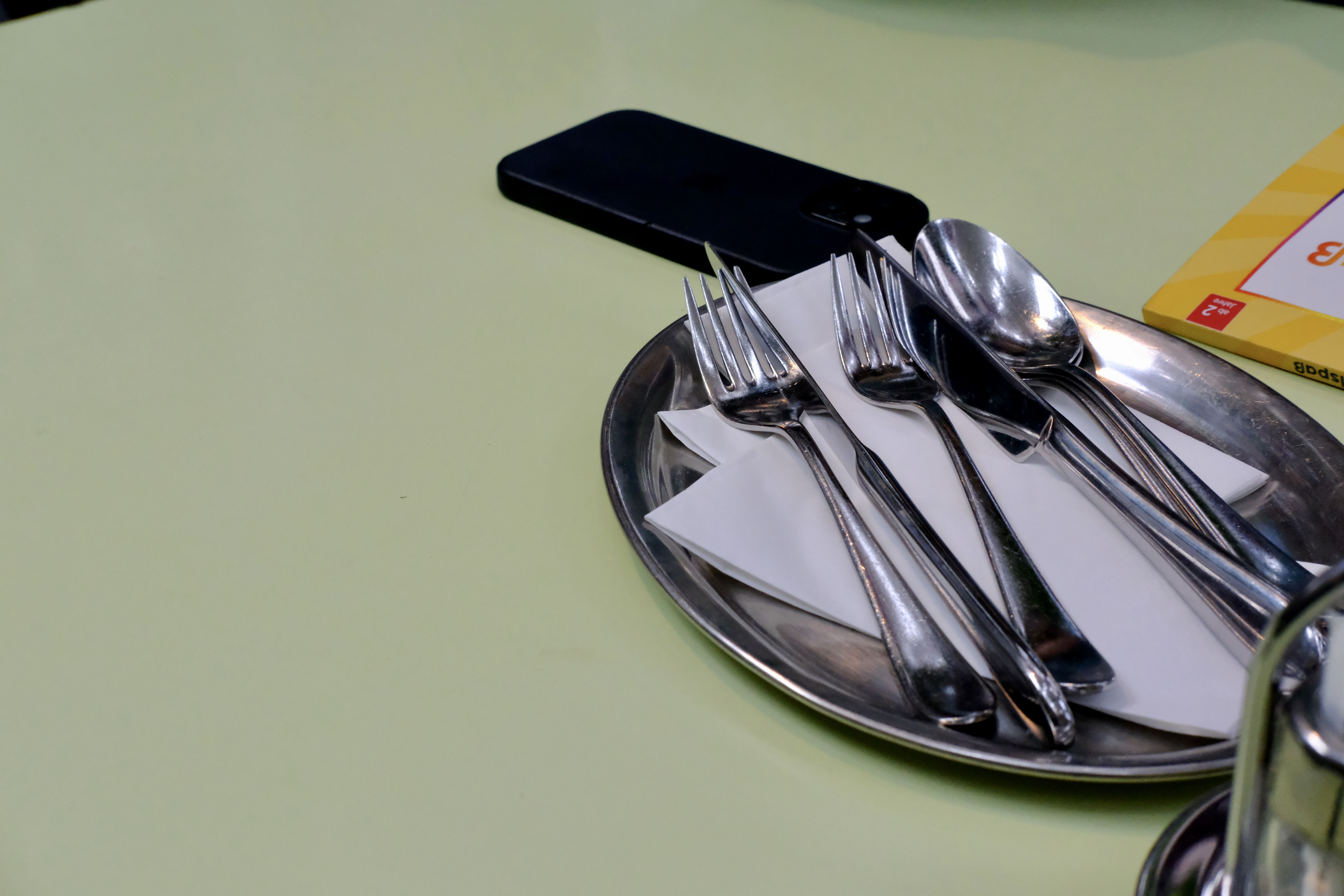 Cutlery on a steel tray, phone face-down on a café table.